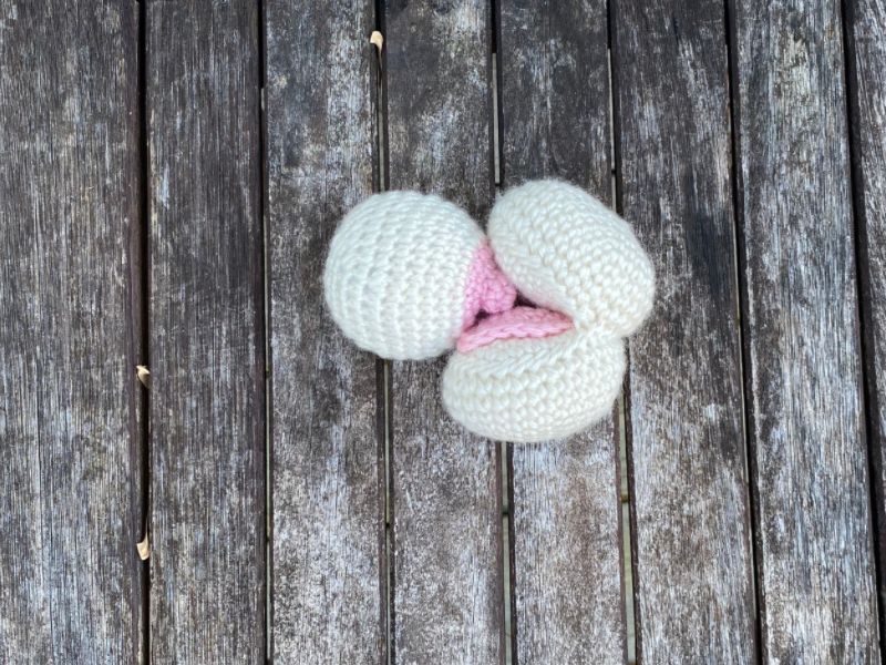 crochet breast and mouth, in off white yarn, with a pink colored nipple and pink colored tongue, laying on a brown faded background