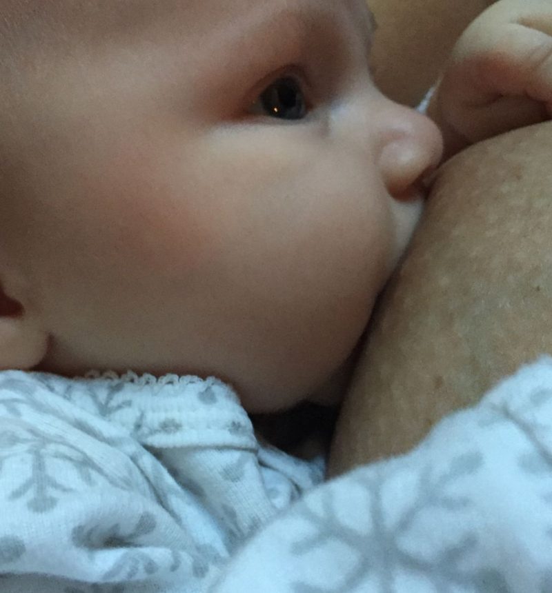 white baby latched onto mother's breast with a white long sleeve onesies with gray snowflakes